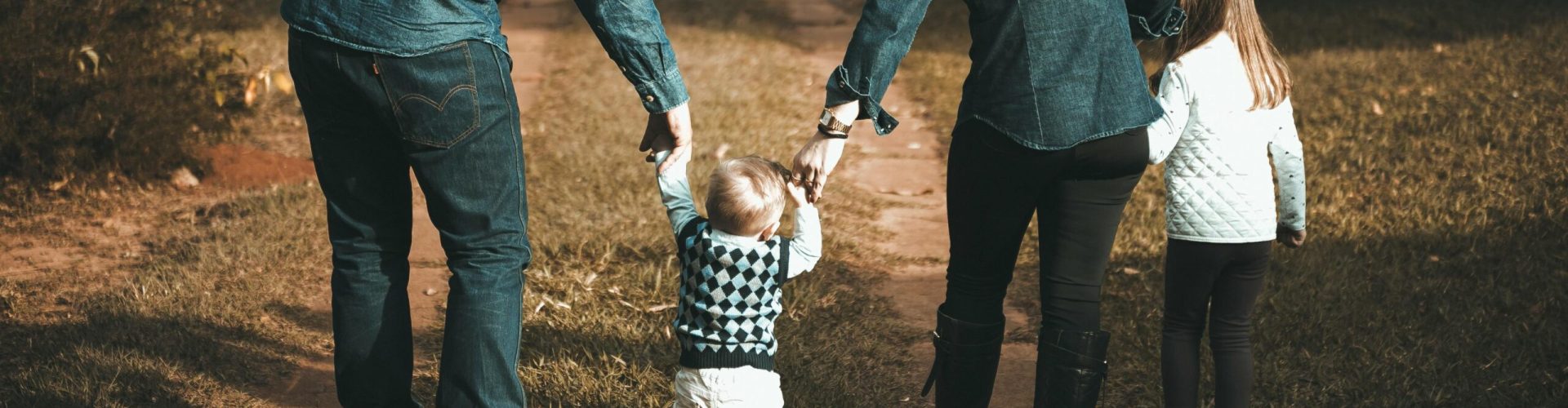 A family of four walks hand in hand on a path, enjoying a sunny day outdoors.